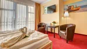 Habitación de hotel con una cama, dos sillones, una mesita, un televisor y un cuadro de una playa.