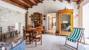 A rustic interior with exposed wooden beams, a stone wall, a wooden dining table with chairs, a large cabinet, and a striped beach chair. - Lovely home in Rosolini SR with private swimming pool, can be inside or outside (Rosolini SR)
