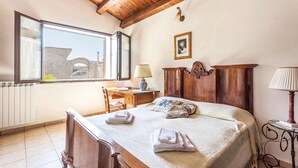 A bedroom with a large bed, wooden headboard, a desk with a lamp, a chair, and a window with a view of a building. - Lovely home in Rosolini SR with private swimming pool, can be inside or outside (Rosolini SR)