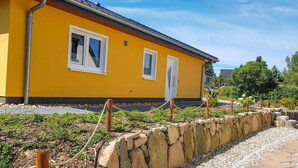 En gul bygning med to vinduer, en stenvæg og en grussti.