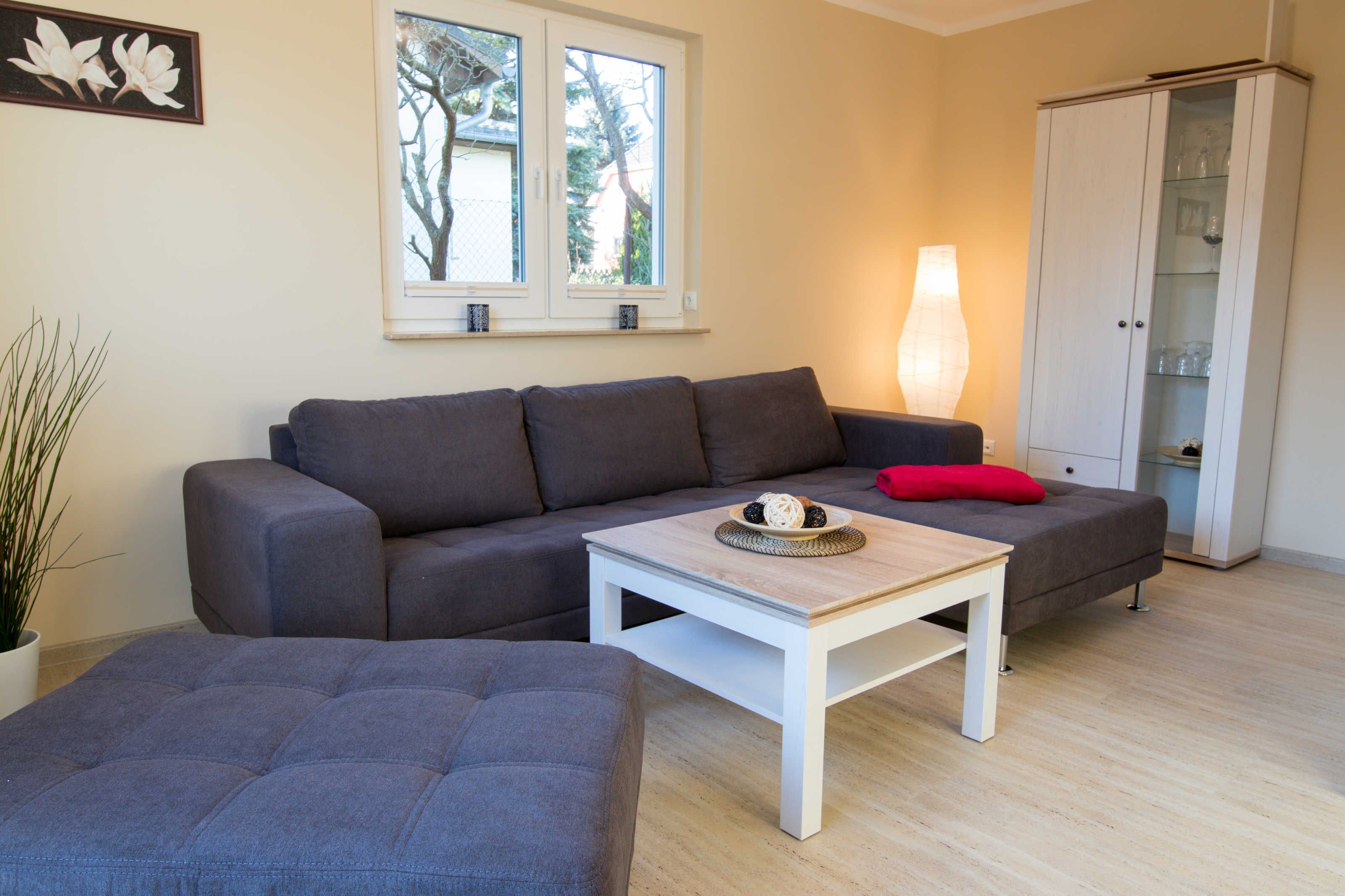 En stue med en grå sofa, et hvidt sofabord, en rød pude, en lampe og et skab med glaslåger.