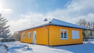 Ein gelbes Gebäude mit schneebedecktem Dach, umgeben von Schnee und Bäumen.