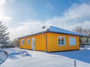 A yellow building with a snow-covered roof, surrounded by snow and trees.