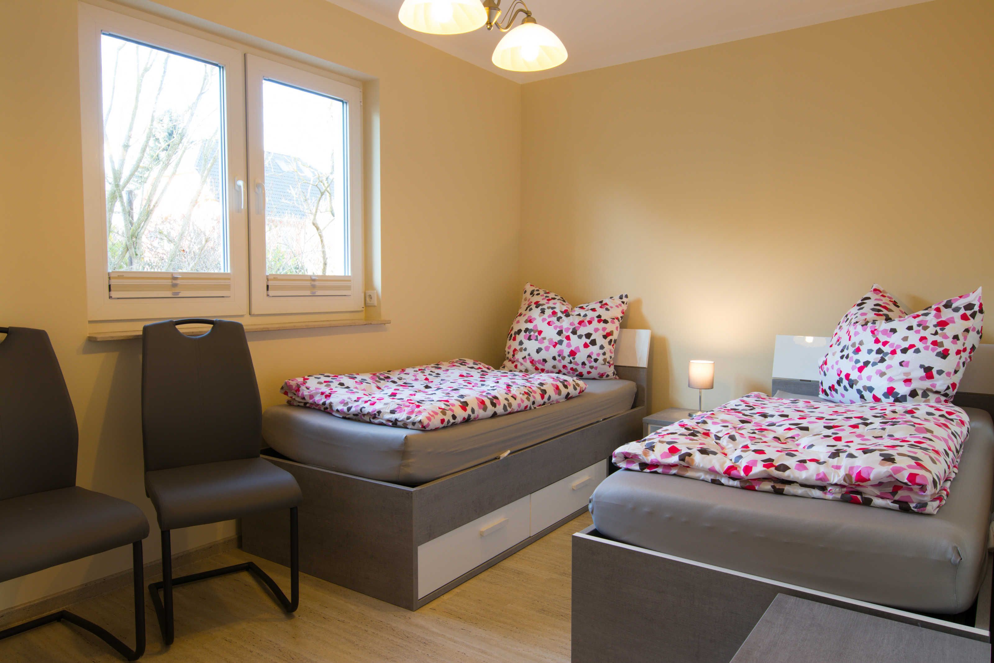Ein kleines Schlafzimmer mit Bett, Sessel, Nachttisch und Fenster.