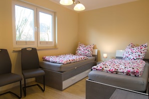 A compact bedroom with a bed, a chair, a bedside table, and a window.