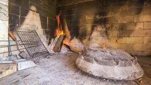 Una chimenea de piedra tradicional con una rejilla de metal y una olla de piedra grande y redonda.