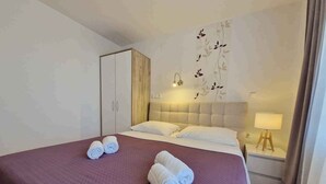 Quarto de hotel com uma cama grande, duas toalhas dobradas, uma mesinha de cabeceira com abajur e um guarda-roupa.