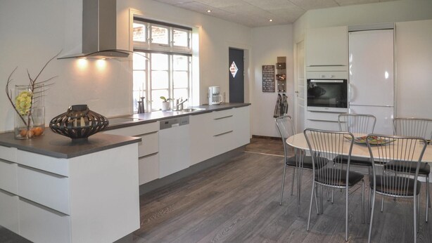 A modern kitchen with white cabinetry, a central island, and a dining area with metal chairs.