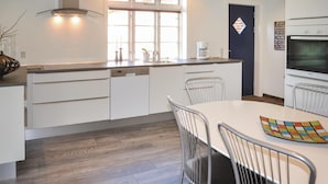 A modern kitchen with white cabinetry, a built-in oven, and a dining area with a white table and metal chairs.