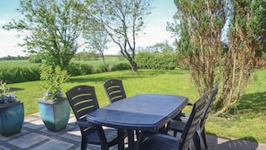 An outdoor patio with a table and chairs, surrounded by greenery and trees.