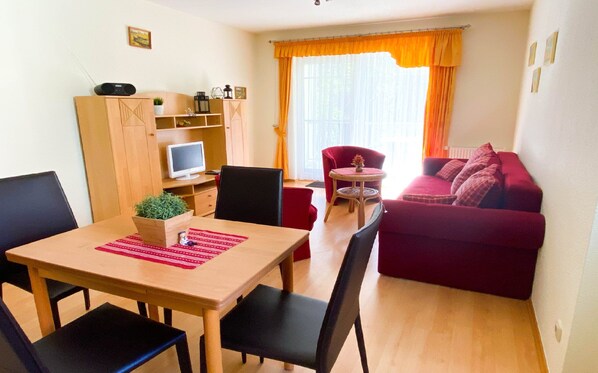 Un espace de vie compact comprenant une table à manger, des chaises, un canapé rouge, un téléviseur et une petite plante.