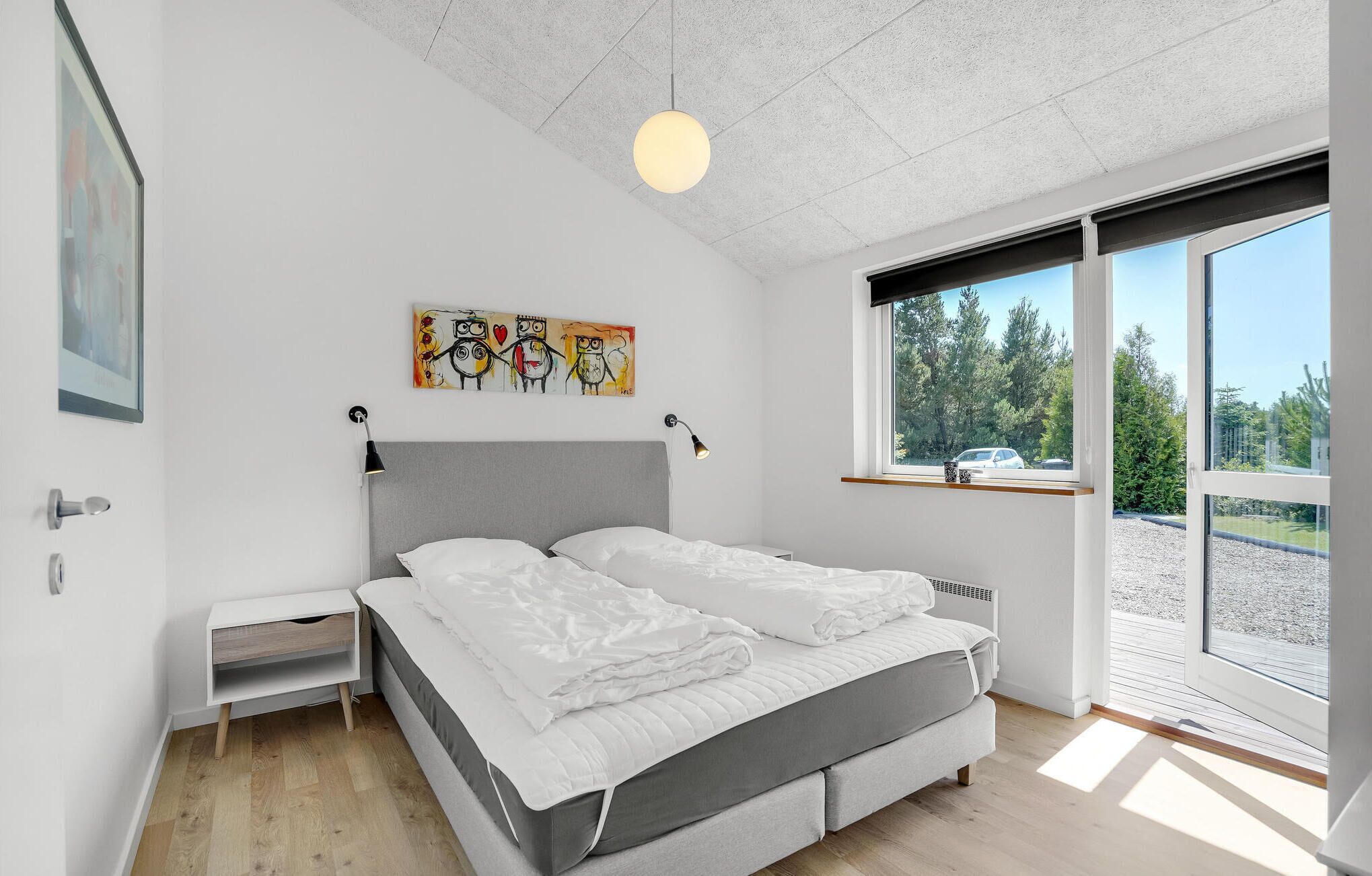 Ein modernes Schlafzimmer mit einem Bett, Nachttischen, einem Gemälde und einem Fenster mit Blick auf Bäume.