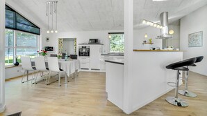 A modern kitchen with white cabinetry, a dining area with white chairs, and a bar area with a stool. - 3 bedroom gorgeous home in Skjern (Skjern)