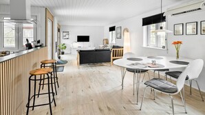 Moderni keittiö, jossa on baaritiski, ruokapöytä tuoleineen sekä oleskelutila, jossa on sohva ja televisio.