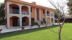 A two-story building with a brick facade, multiple balconies, and a well-maintained lawn. - Holiday apartment with air conditioning (Malinska)
