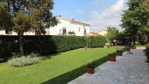 Ein gepflegter Garten mit einem Kiesweg, ordentlich gestutztem Rasen und verschiedenen Pflanzen in Töpfen.