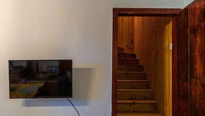Uma escada com degraus de madeira descendo para um nível inferior, uma TV de tela plana na parede e um interruptor de luz na parede.