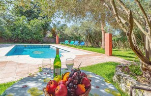 A poolside table with a bottle of wine, glasses, and a fruit basket. - Beautiful home in Montecorto with WiFi (Montecorto)