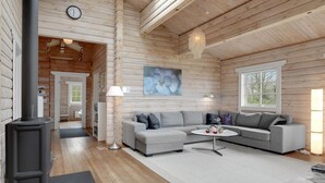 Interior acollidor d'una cabana de fusta amb un sofà seccional gris, una taula de centre rodona i una finestra gran.