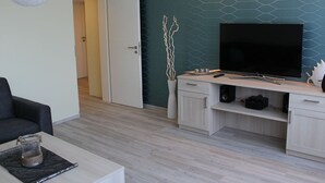 A modern living room with a flat-screen TV, a dining table, and a sofa. - Densee: Ferienwohnung Süderende - Apartment (Insel Hiddensee)