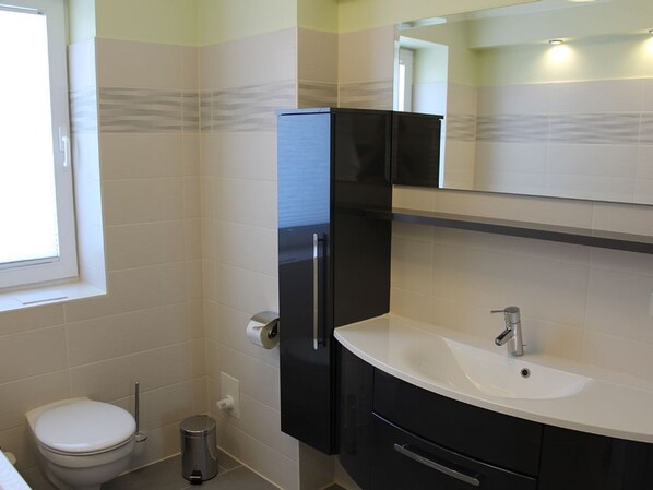 Une salle de bain équipée de toilettes, d’un lavabo, d’un miroir et d’une poubelle.