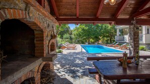 Zona de piscina con horno de ladrillo, sillas de descanso y una mesa con una botella y vasos.