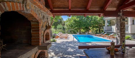 A pool area with a brick oven, lounge chairs, and a table with a bottle and glasses.