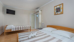 Habitación de hotel con dos camas individuales, cabecero de madera, televisor montado en la pared y un cuadro colgado.