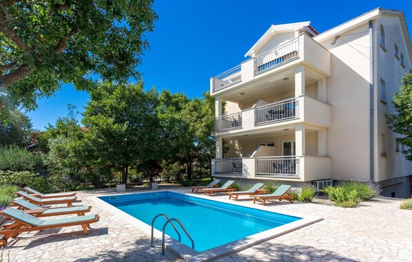 A modern multi-story building with a swimming pool, outdoor seating, and lush greenery.