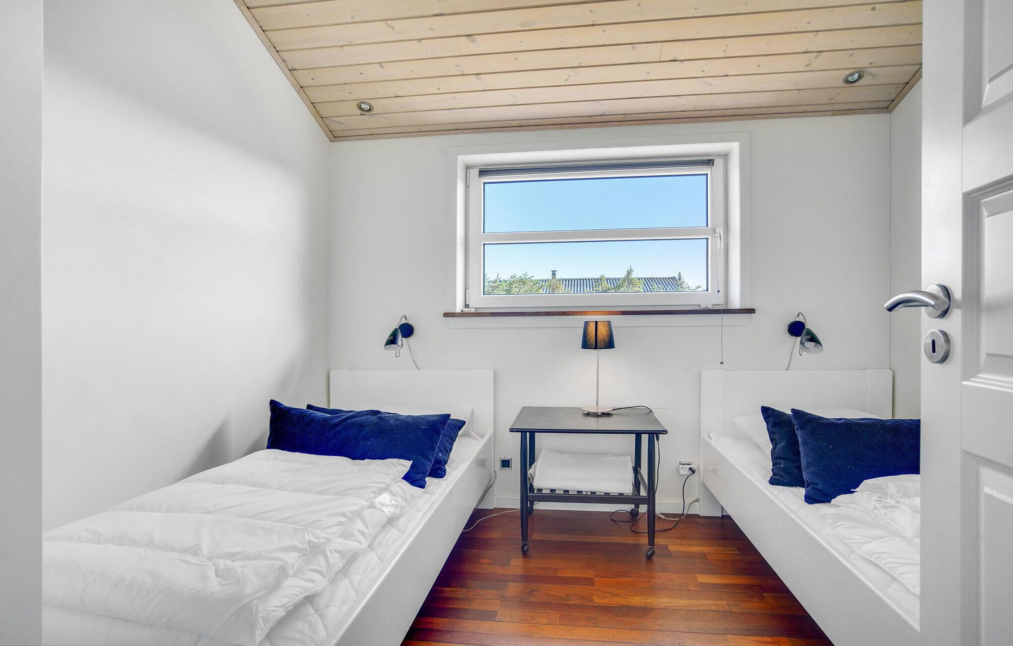 Une petite chambre propre, avec deux lits simples, un bureau et une fenêtre donnant sur l’extérieur.
