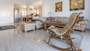 A spacious living room with a sofa, ottoman, and a wicker rocking chair. There is a dining table with chairs and a kitchen area in the background. - Amazing home in Ciudad Quesada-Rojales (Ciudad Quesada-Rojales)