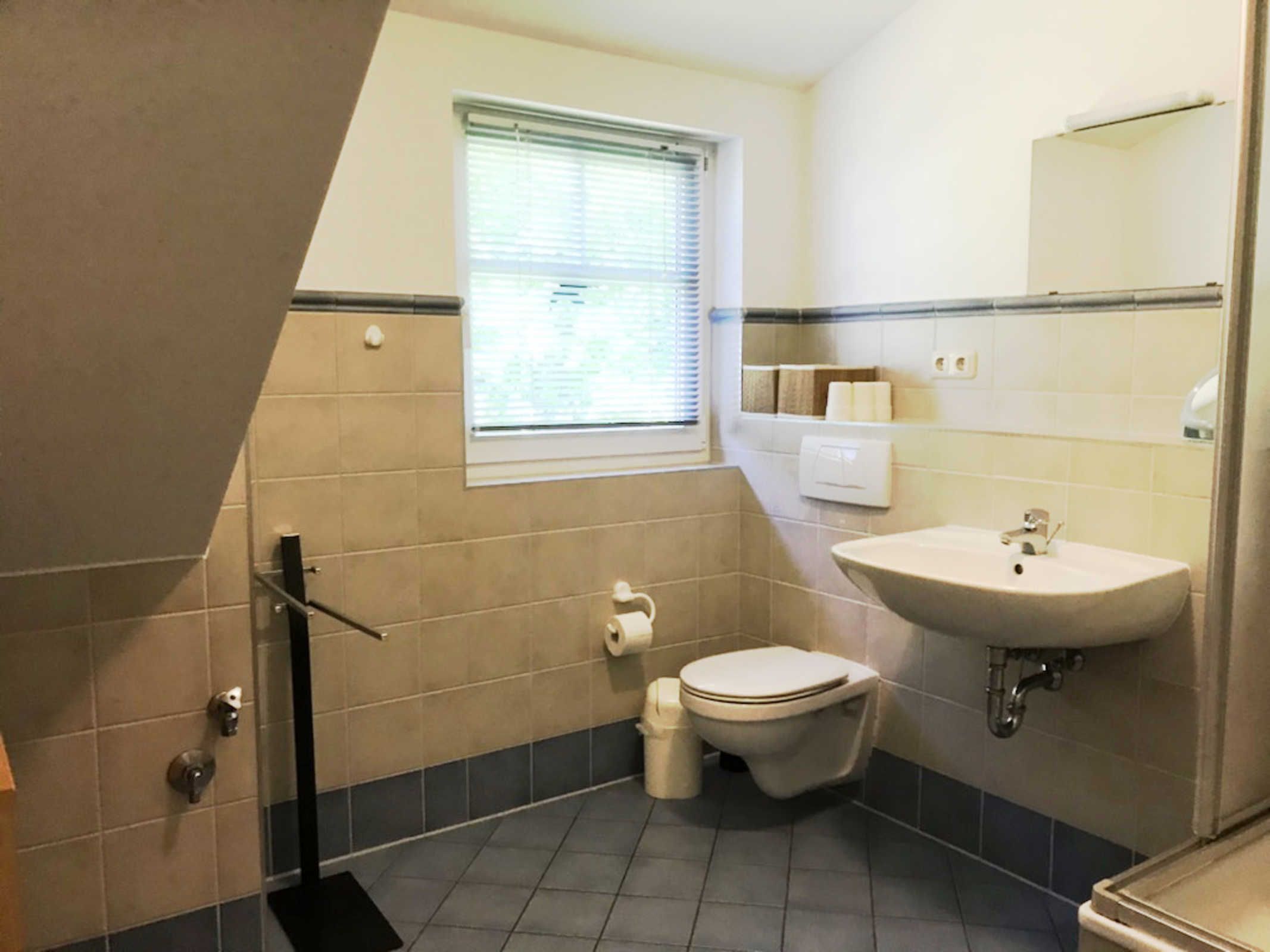 A bathroom with a toilet, sink, window, and towel rack.