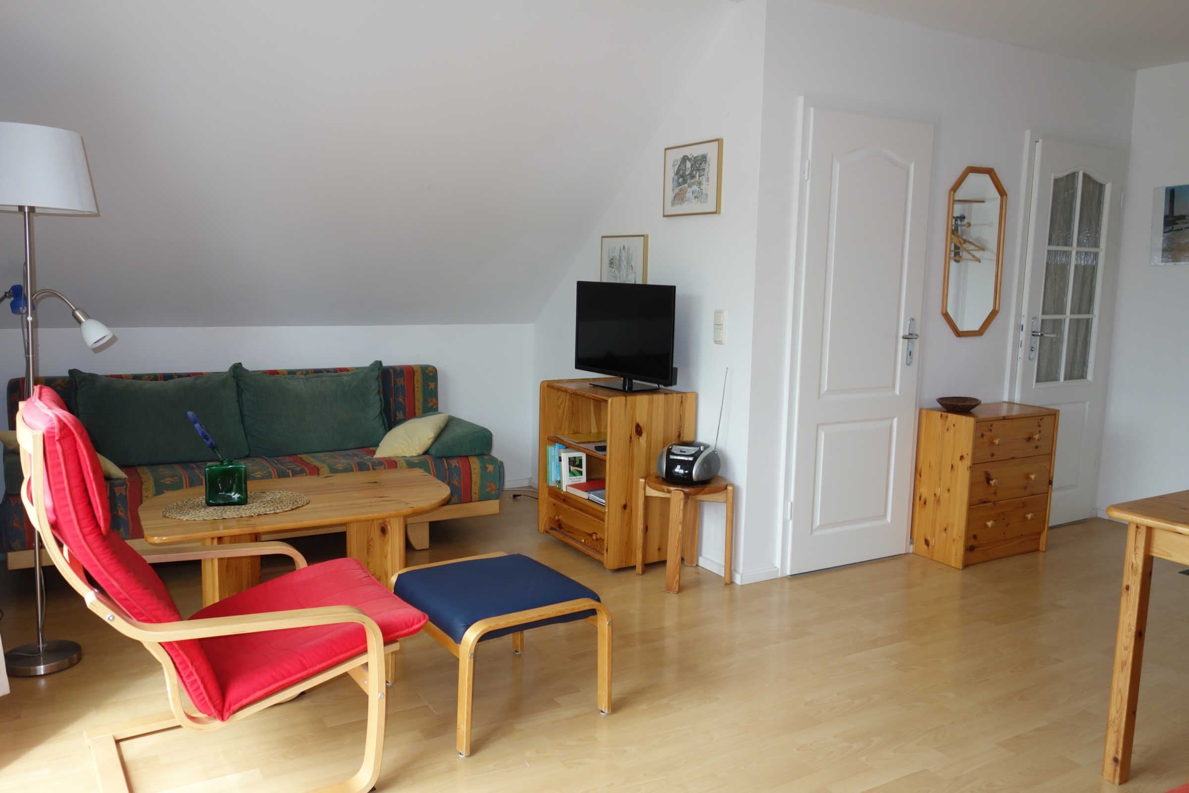 A living room with a sofa, a red chair, a wooden table, a television, and a cabinet.