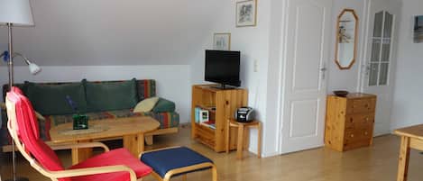 A living room with a sofa, a red chair, a wooden table, a television, and a cabinet.
