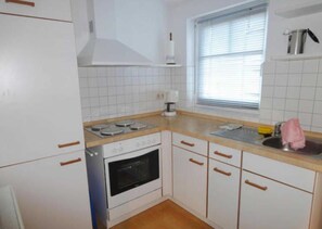 A kitchen with white cabinets, a stove, an oven, a window with blinds, and a sink with a towel.