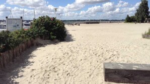 Ein Sandstrand mit einer Holzlattenzaun, einem Schild und einem klaren Himmel mit Wolken.