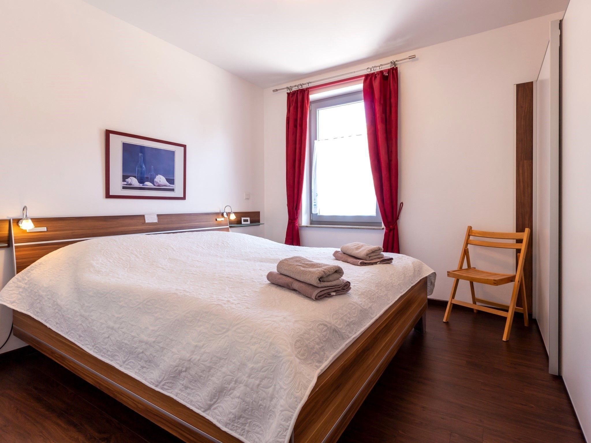 A neatly made bed with a white duvet, a wooden headboard, and a bedside lamp.