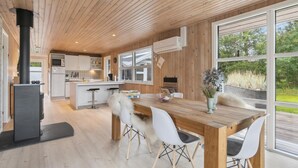 Una cocina moderna con detalles de madera, un comedor con sillas blancas y ventanas amplias que ofrecen vistas al exterior.