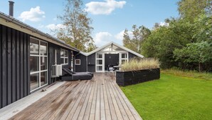 Una casa moderna con terraza de madera, ventanas amplias y jardín.