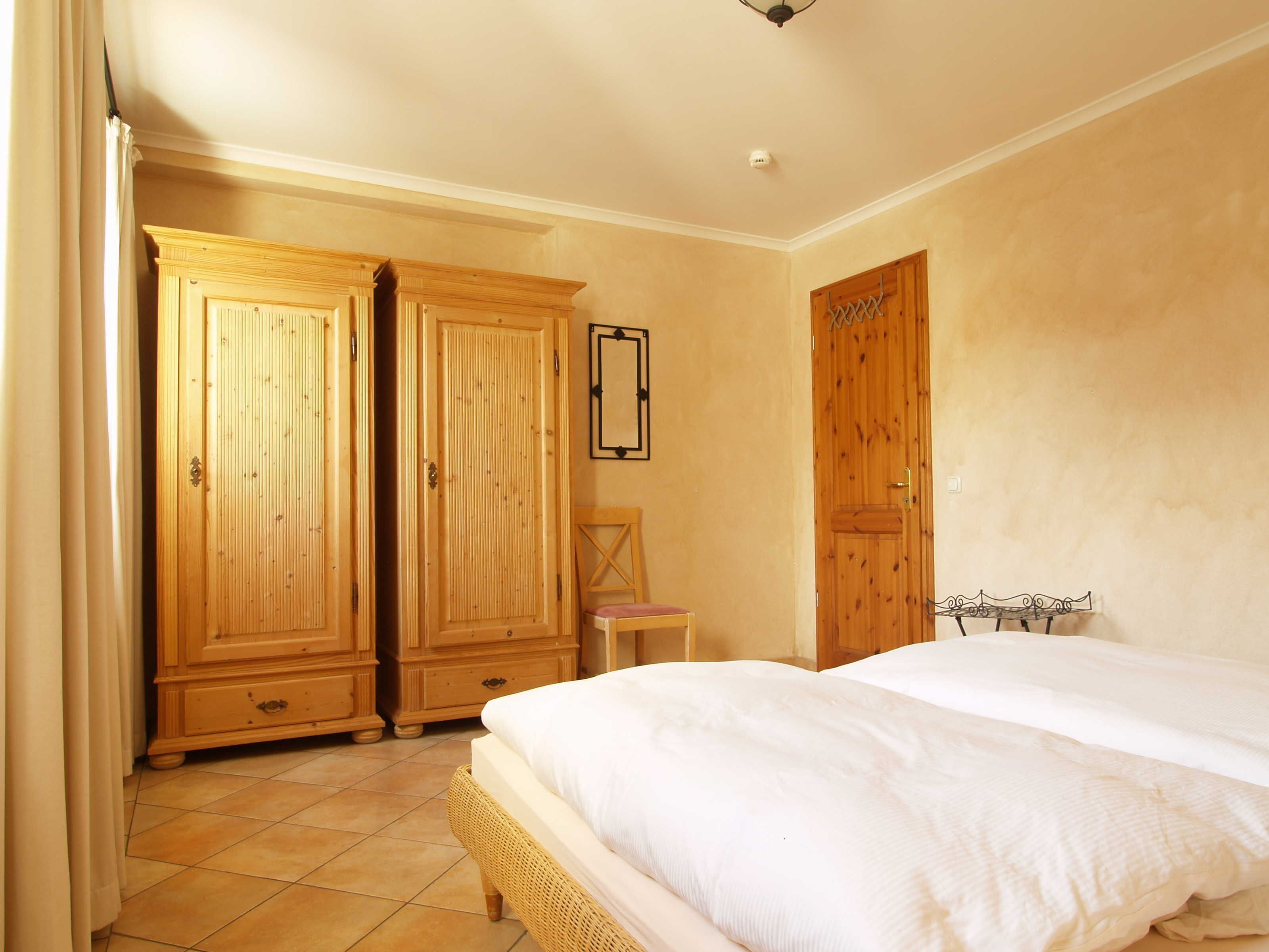 Ein Schlafzimmer mit einem großen Bett, Holzschränken, einem Sessel und einem kleinen Tisch.