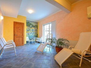 Una habitación iluminada por el sol con un mural, una puerta de madera y varias sillas blancas.