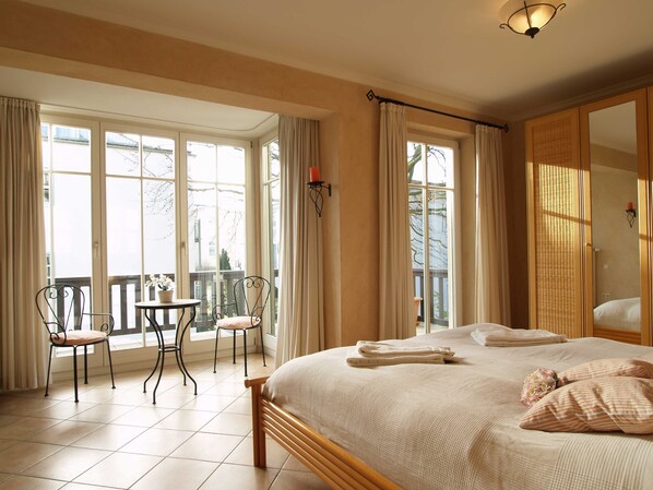 Une chambre avec un grand lit, un balcon avec des chaises et une vue sur l’extérieur.
