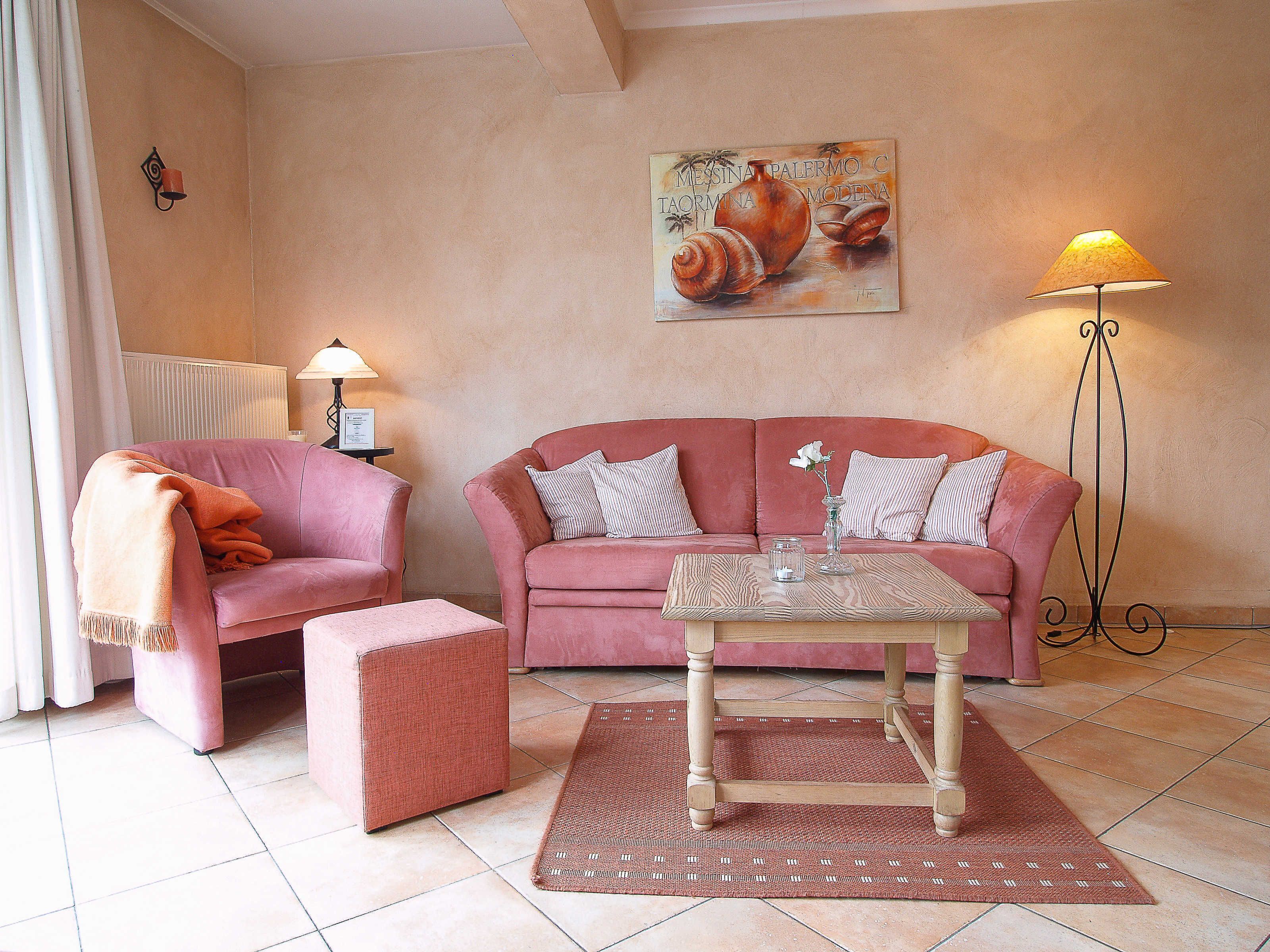 A living room with a pink sofa, a matching armchair, a glass coffee table, and a floor lamp.