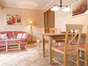 Una sala de estar acogedora con un sofá, una mesa de comedor con sillas, una lámpara de pie y obras de arte en las paredes.