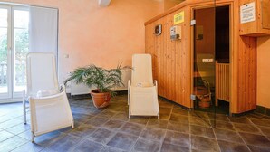 Ein Zimmer mit einer hölzernen Sauna, einem weißen Stuhl, einem Blumentopf und einer Glastür, die auf einen Balkon führt.