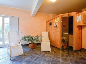 Ein Zimmer mit einer hölzernen Sauna, einem weißen Stuhl, einem Blumentopf und einer Glastür, die auf einen Balkon führt.