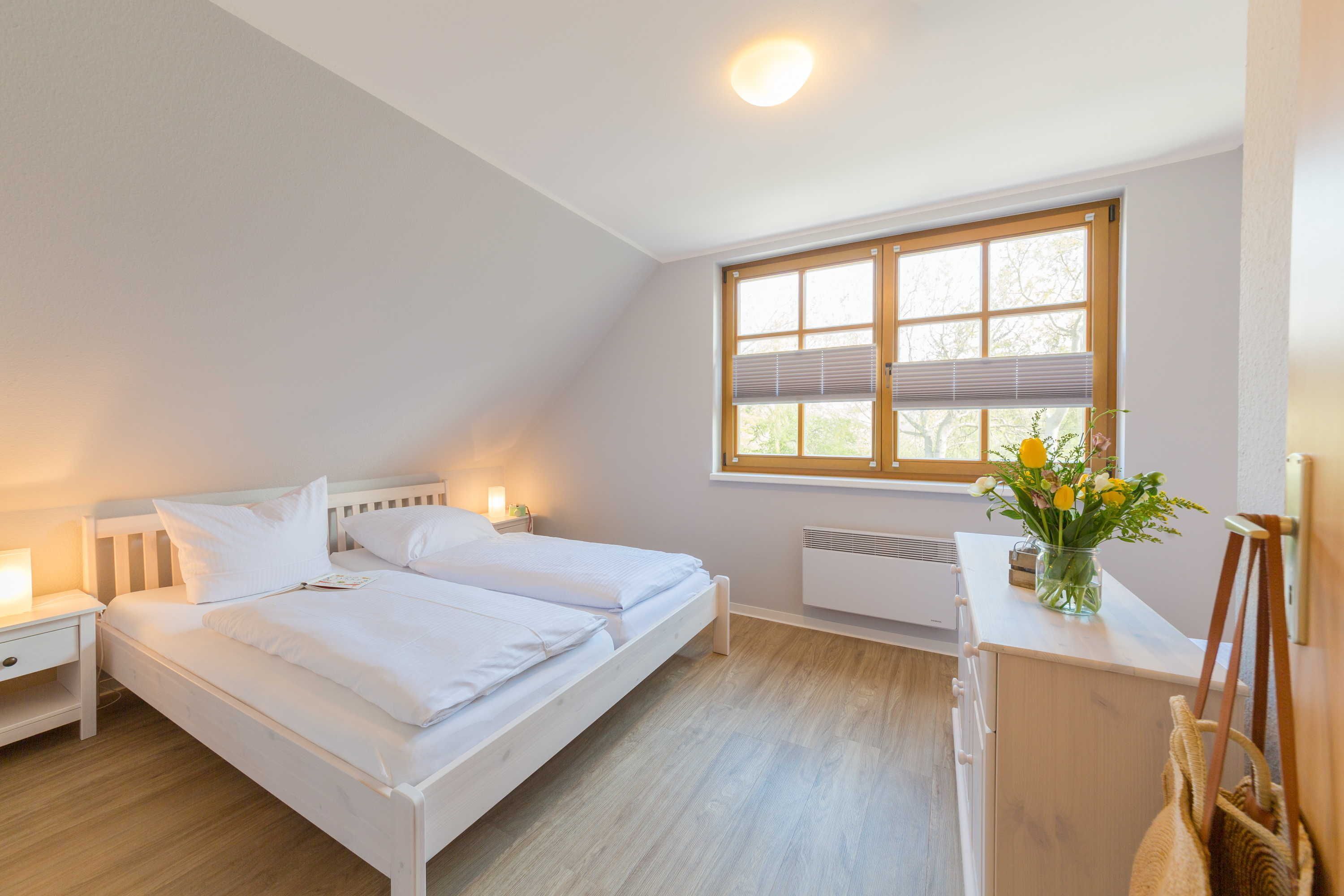 Ein Schlafzimmer mit zwei Betten, einem Nachttisch mit Lampe, einem Fenster mit Jalousien und einer Heizung.