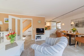 A modern living room with a sofa, a dining table, and a TV. There is a staircase leading to another level.