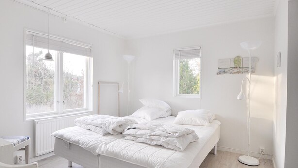 A minimalist bedroom with a large bed, two windows, a radiator, and a bedside table.