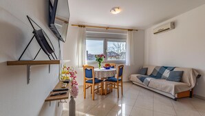 A living room with a sofa, a dining table with chairs, a TV mounted on the wall, and a window with curtains. - 2 bedroom cozy apartment in Medulin (Medulin)